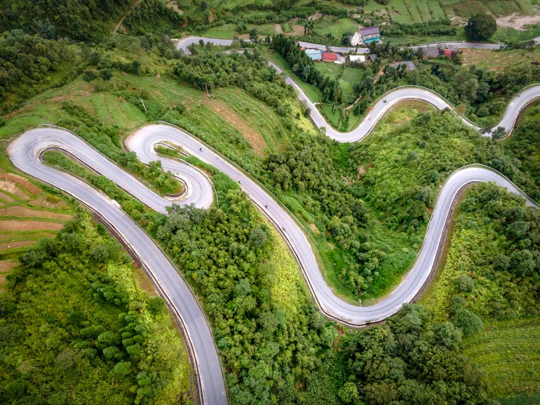 Aerial view of a winding mountain road through green forest